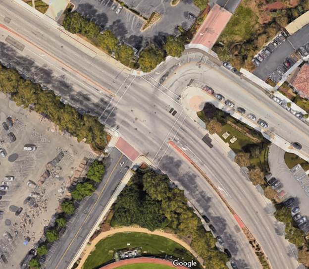 Aerial view of an intersection with no driveway entrances in the functional area of the intersection. There are driveways leading to parking lots visible in the image, but they are farther away from the intersection.