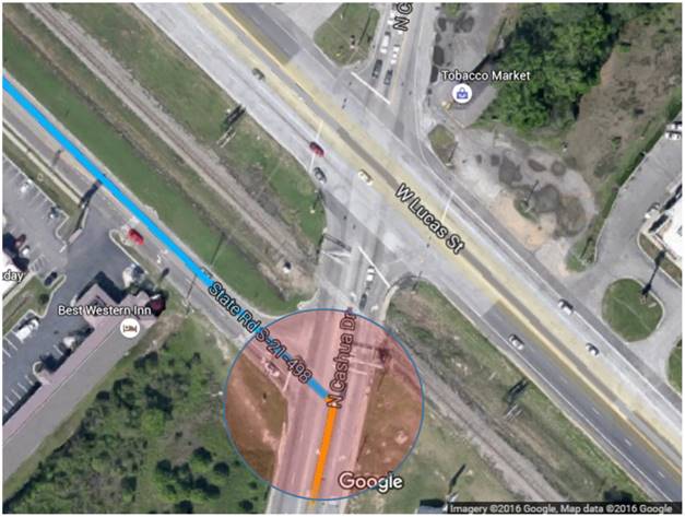 Bird’s-eye view of a three-legged stop-controlled intersection. The cross streets are labeled, and a transparent red circle highlights the intersection being verified. Just north of the intersection, along the main roadway, there is a railroad crossing followed by a signalized intersection with a major roadway.