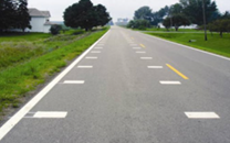 This is a photo of a two-lane road with white transverse pavement markings on both sides of the travel lane.
