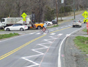 This is a photo of a two-lane road with white zigzag pavement markings. These markings are painted in the travel lane to indicate horizontal curves or crosswalks.