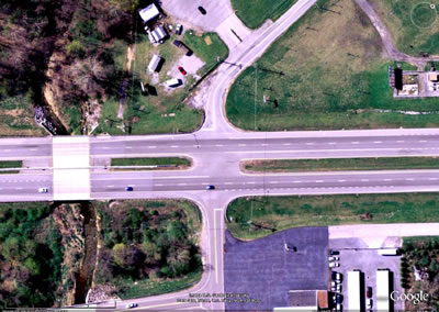 Figure 6. Photo. The conventional intersection observed in this study. This photo shows a satellite view of the conventional intersection observed in this study. Turning movements were observed so that conflicts between vehicles at the restricted crossing U-turn could be compared to conflicts at a nearby conventional intersection. The four-lane divided highway is crossed at a right angle by a two-lane rural road. There is no acceleration lane for vehicles turning right from the minor road. There are deceleration lanes for vehicles turning left off of the highway from either direction. There is a wide opening in the median to accommodate all left-turn and through movements on the minor road.
