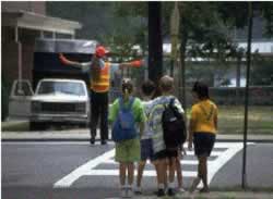 Figure 37. Studies have found that uniformed crossing guards, such as the one above wearing a reflective vest while signaling traffic to allow a group of school children to cross, are safer than other control devices such as signs or markings alone