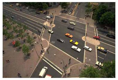Use of colored crosswalks and median refuges makes this intersection more pedestrian-friendly. This is an aerial photograph of a wide intersection of a seven-lane major road with a four-lane minor road. Crosswalks are defined at each approach using colored paver stones, and refuge islands at the center of the major road make crossing the wide roadway less of a challenge.