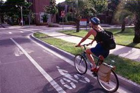 3) This photograph shows a bicyclist riding in a bike lane, which is separated from the vehicle travel lane by a solid white tranverse pavement marking. A bike symbol pavement marking is also visible in the bike lane.