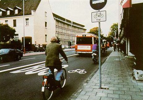 The photograph shows a travel lane in Germany being shared by a bus and a bicyclist. Pavement markings in the lane have the text 'BUS' on the left side of the lane (inside of the road) and a bike symbol on the right side of the lane (outside of the road).