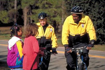 The photograph shows two uniform bicycle patrol officers stopped and talking with two young girls.