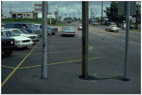 Parked cars and a lack of sidewalks along the road’s edge create unsafe conditions for bicyclists and pedestrians.