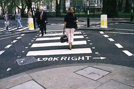 This picture shows a pedestrian crosswalk that has wide painted bars parallel to the direction of vehicle travel. Several people are crossing the street, and the text "LOOK RIGHT" is painted on the street next to the curb.