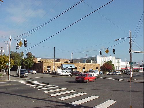 This photo shows the intersection of a major roadway with a minor one and a continental-style crosswalk going across the major road. Above the major road is a span wire with two signal heads in each direction and a pedestrian sign to warn motorists of pedestrian presence.