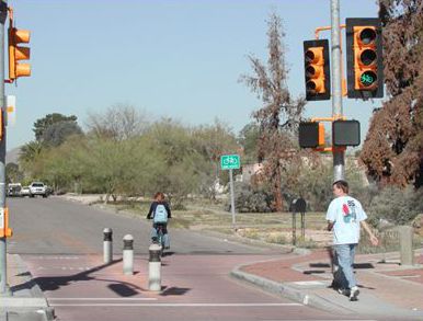 This picture shows a bicyclist and pedestrian traveling along a bicycle boulevard. At the intersection, motor vehicle traffic is not permitted to travel straight across the intersection. Instead, motor vehicle traffic is forced to turn right.