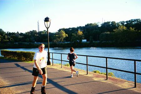 Picture shows a broad shared use path along a river. A woman is jogging away from the viewer and there is a man rollerblading in the direction of the viewer.