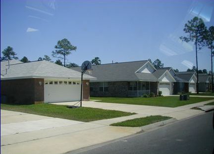 Picture shows repetitious suburban homes where the garages face the street. There are no street trees. There is no visual interest.