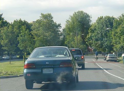 Picture shows cars on a narrow, one-way traffic road. There is a bike lane and one cyclist rides in the distance.