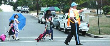 The second picture shows a crossing guard in a crosswalk, helping a few school children and their parents cross the street.