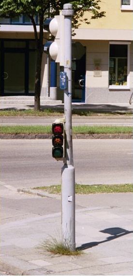 The photograph shows a bicycle signal with a bike symbol and an arrow. The bicycle signal is considerably smaller than a standard traffic signal and is mounted on a mast arm pole.