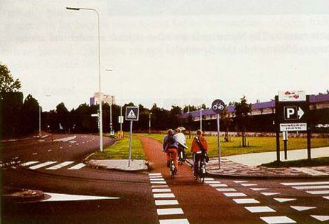 The photograph shows a bicycle path that parallels the main road. There is physical separation between the road and bike path with has been planted with grass.
