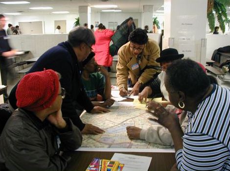 The picture shows six people clustered around a map, taking notes in a planning session.