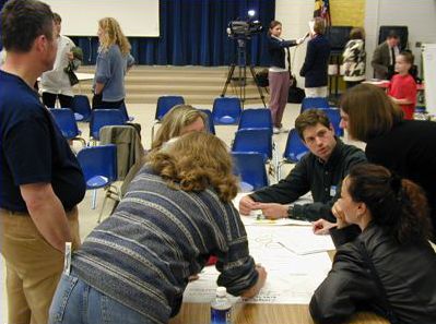 The picture shows six people clustered around a map, taking notes in a planning session.