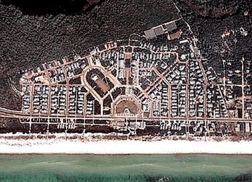 Picture shows an aerial view of a new urbanist neighborhood with one side facing the beach and ocean. The plan has a central town green and village center. The streets are in a modified grid showing dispersed uses. One main street goes through the town center, but the neighborhoods can easily avoid it.
