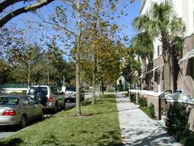 The pedestrian perspective and shows a sidewalk in front of homes and a tree lined grass strip between the street and sidewalk.