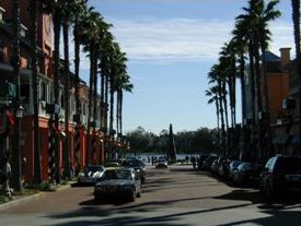 The second photo is of a wide street lined with tall palm trees that runs in front of store fronts. Cars are parked at the curb on both sides of the street. 