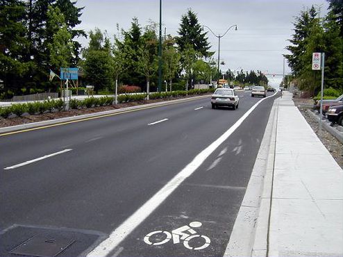 This picture is of the same road as the previous slide after improvements. The improvements include a sidewalk, bike lane and four lanes of traffic divided by a landscaped median.
