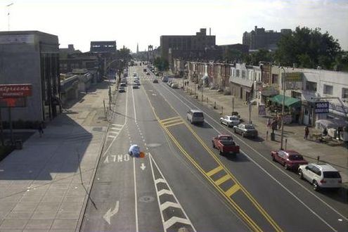 Picture shows the same street as the previous slide with improvements. There are now two travel lanes with on street parking. Bike lanes have been added. Left and right turn lanes have been added at intersections. The center lane is now a turn lane and has stripes running across it to deter travel in that lane.
