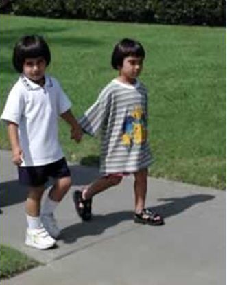 Picture shows a two toddlers holding hands while walking on a sidewalk.