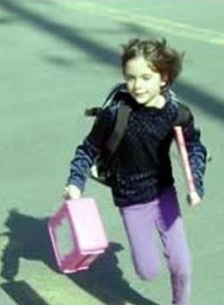 Picture shows a young girl running with a lunchbox and books in her hands.