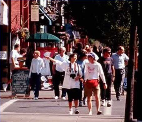 The picture shows a busy street crossing with numerous adults crossing and walking along a sidewalk.