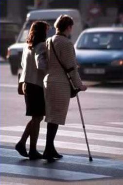 The second picture on the right of the slide shows a woman with an arm–braced cane crossing a street with the assistance of another adult.