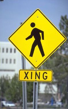 This picture shows a pedestrian crossing sign that has a symbol of a person walking, with a supplemental plaque below that has the text "XING".