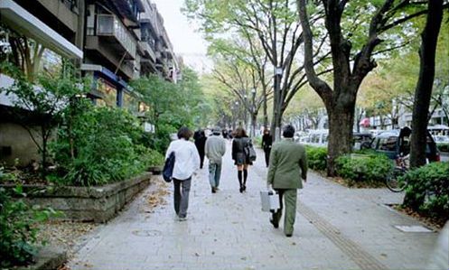 This picture shows several people walking along a wide sidewalk.