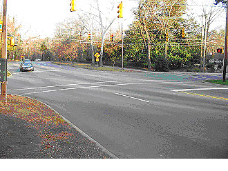 Figure 12. Photograph. Diagonal view of pedestrian example intersection. This is one of three photographs of the same intersection. This picture, from the street level, shows the signalized intersection of two roads, a four-lane main road and a two-lane cross street in a predominantly residential area. This picture shows the same crosswalk as in Figure 11 from farther down the main street (the crosswalk is marked by an arrow pointer).