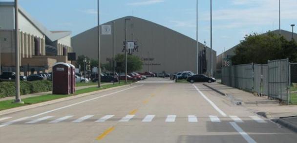 This photograph shows a closeup of an existing midblock site with continental markings. The continental crosswalk spans a two-lane campus street at Texas A&M University. Pedestrian crossing warning signs on approach are not visible in this photo.
