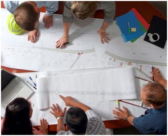 A group of five people is gathered around a table inspecting charts and graphs of collected data.