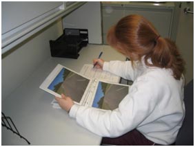A research participant sits at a table looking at images and filling out a survey on paper. There is no experimenter involved with the participant.