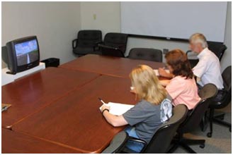 Three study participants are seated at a table and are viewing a roadway scene on a monitor. They are filling out a written comprehension study.