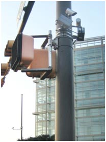 A pedestrian volume counter is mounted on a traffic signal post. The device is small with several pieces of equipment.