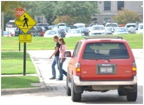 Two pedestrians use a gap in traffic to cross a street in front of a motor vehicle.