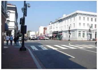 Figure 2. Photo. Example of a signalized intersection. This photo shows an example of a signalized intersection. Several lanes are visible in both directions, as well as crosswalks and traffic signals. There are sidewalks and buildings on both sides of the street. Pedestrians are seen crossing the street at one of the crosswalks.