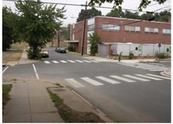 Figure 4. Photo. Example of a partially stop-controlled (one- or two-way) intersection. This photo shows an example of a partially stop-controlled (one- or two-way) intersection. There is a four-way intersection with four crosswalks. One stop sign is visible on the right-hand side. There are buildings and sidewalks on all sides of the intersection.