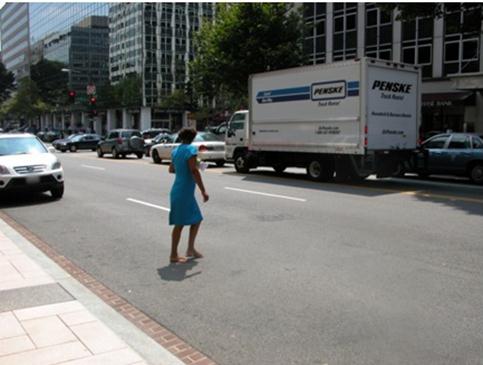Figure 7. Photo. Example of a midblock location with no crosswalk. This photo shows an example of a midblock location with no crosswalk in an urban setting. A pedestrian is seen crossing in the middle of a busy street with no crosswalk. There are motor vehicles traveling in both directions.