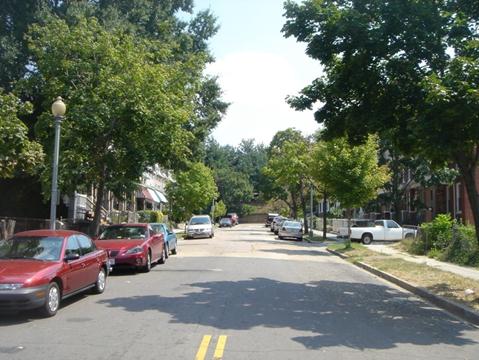 Figure 13. Photo. Example of a playing/working in the roadway location. This photo shows a residential street with one lane in each direction. There are cars parked on the street next to the curb, and there are houses with driveways and sidewalks on both sides of the street.