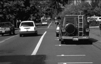 photo of a car going down the road next to cars parked along a curb