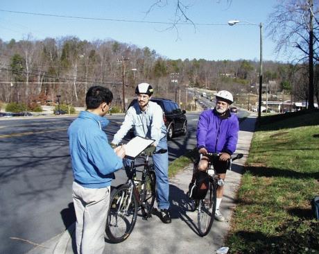 Photo of a person surveying 2 bicyclists on the side of the road