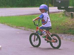 Picture of young child riding bicycle on sidewalk.