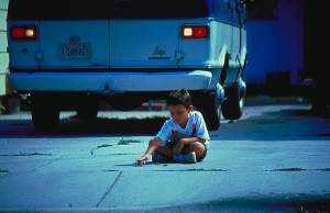 Picture of young boy sitting on ground behind a parked vehicle preparing to back up.