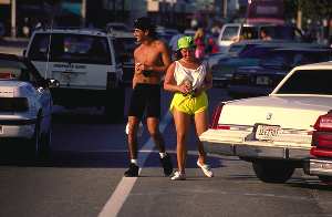 Picture of a man and woman drinking alcohol while walking through traffic.