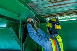 Photo of a man in a hard hat and safety vest attaching a sensor to a horizontal beam under a bridge surface.